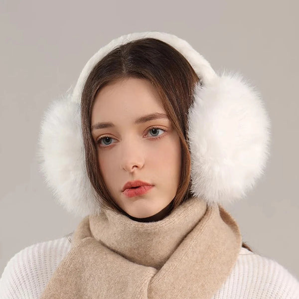 A woman wearing white knitted clothing and a beige faux fur scarf, with fluffy white faux fur earmuffs visible.