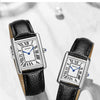 Nahaufnahme einer silbernen, quadratischen Armbanduhr mit schwarzem Lederband auf einer hellen Oberfläche.