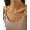 Gros plan d'une femme portant un collier doré avec une lettre et une croix sur un haut beige.