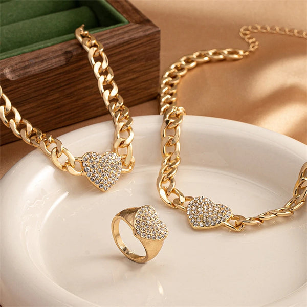 Gold chain necklaces and a ring featuring rhinestone heart charms displayed on a white plate.