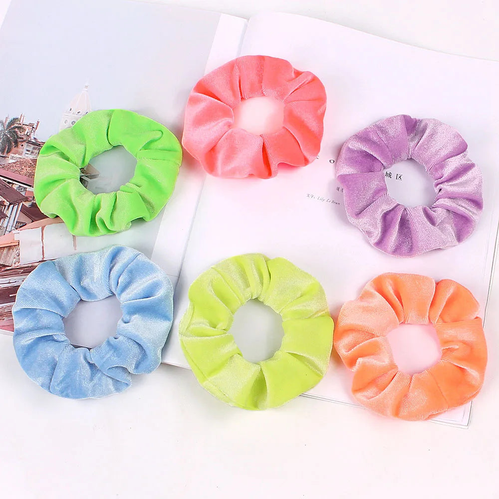 A set of six velvet scrunchies in various shades including pink, purple, green, and orange, displayed on a white background.