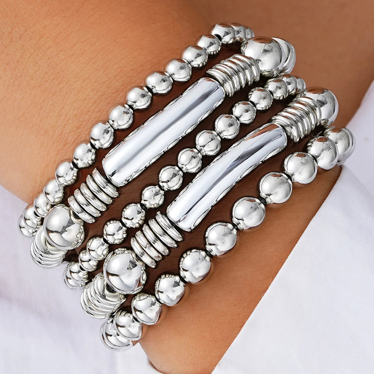 A set of silver and gold-toned beaded bracelets stacked on a person's wrist.