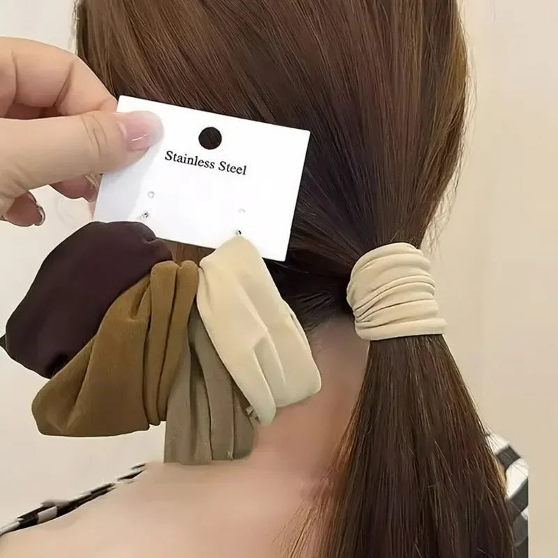 A hand is placing a black tag with the text Stainless Steel onto a brown ponytail, next to several beige and brown elastic ha