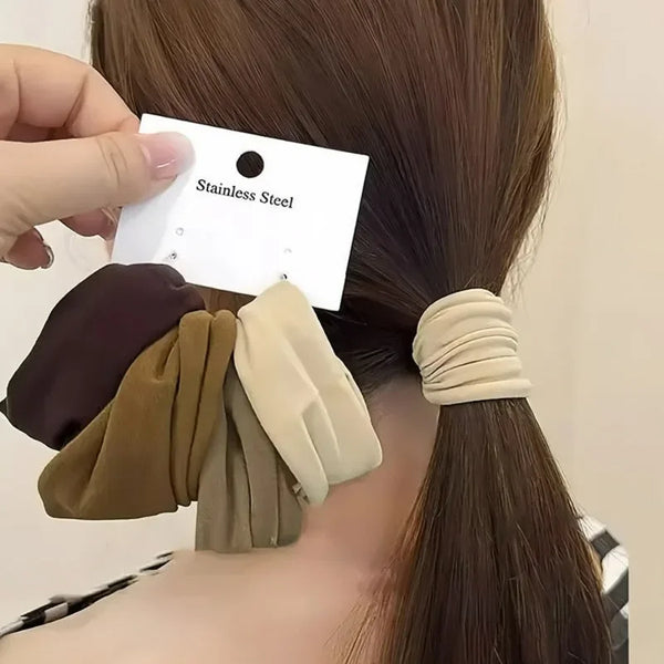 A hand is placing a black tag with the text Stainless Steel onto a brown ponytail, next to several beige and brown elastic ha