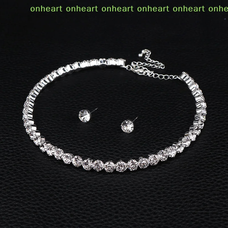 A silver-toned necklace and matching earrings set with clear crystals displayed on a black background.