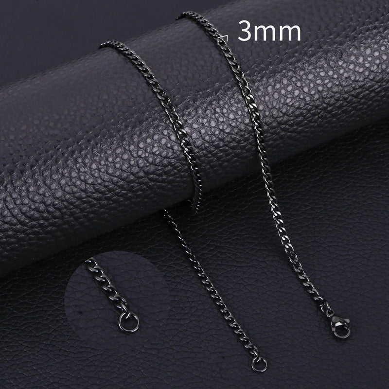 A set of black stainless steel Cuban link necklaces displayed on a dark leather surface.