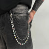 A silver chain necklace with pearl and gemstone beads is hanging from a keychain on dark denim fabric.