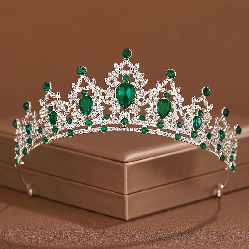 Diadema de cristal plateado brillante con piedras esmeralda, sobre una caja marrón.