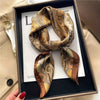 A luxury silk scarf in gold and beige tones is displayed in a black frame.