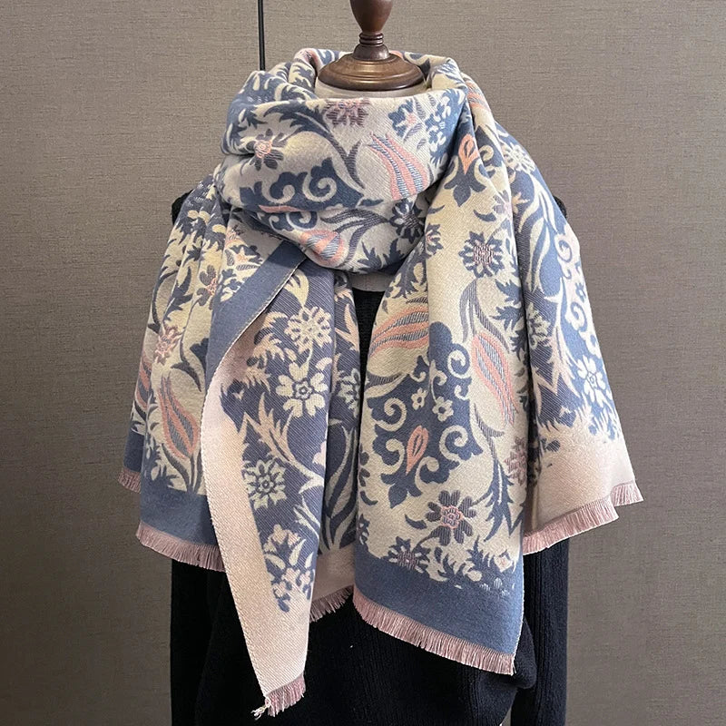 A patterned scarf and shawl wrap in blue, beige, and pink tones displayed on a wooden hanger.