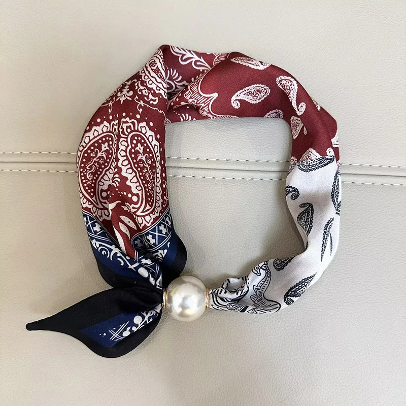 A patterned scarf featuring maroon and white paisley designs tied with a navy blue fabric and a pearl tail magnetic clasp.