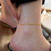 Gros plan d'un bracelet de cheville doré, tiré, porté à la cheville d'une personne.