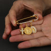 Eine Hand hält eine goldfarbene St. Benedikt-Medaille-Anstecknadel mit Kreuz und Figur auf einer Kette.