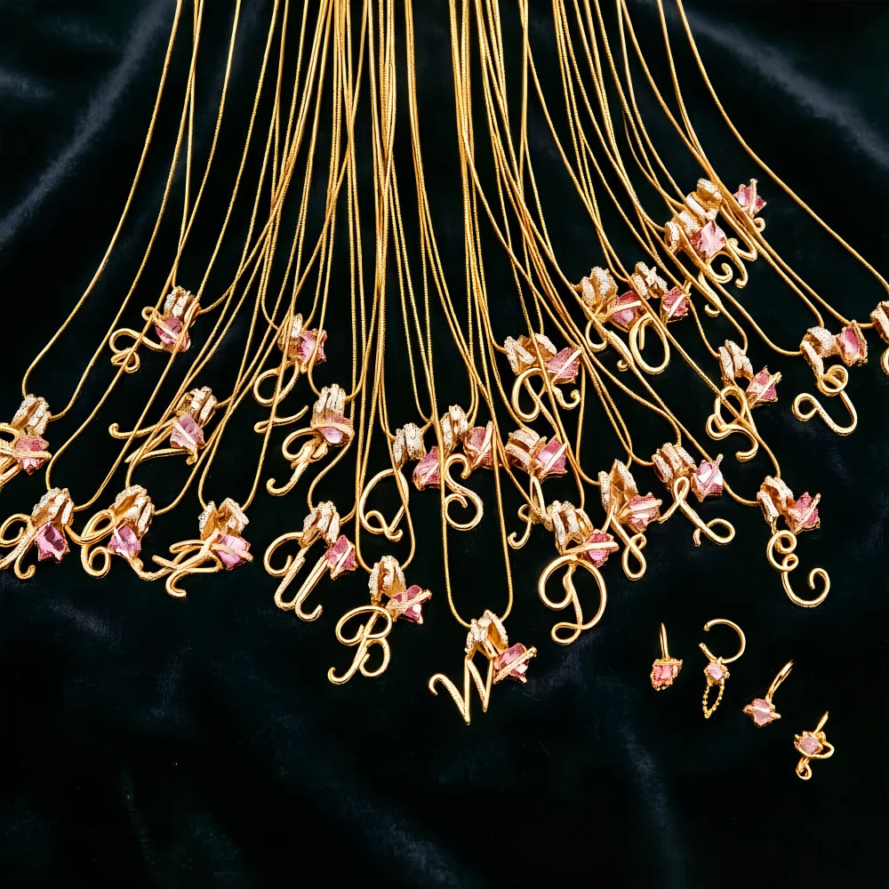 A cascade of gold alphabet letter pendants with pink flowers hanging against a black velvet background.