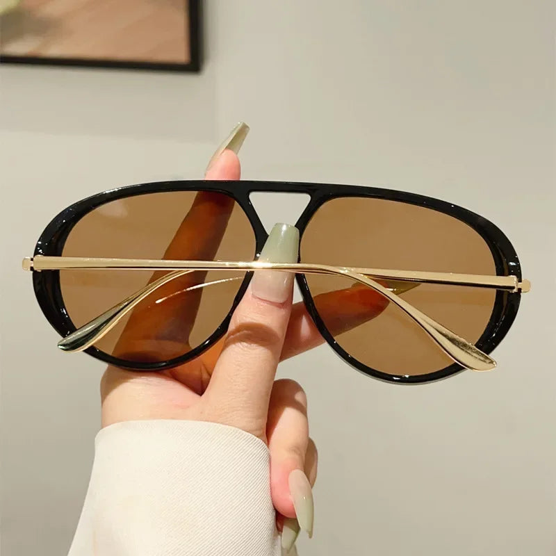 A hand holds a pair of aviator style UV protection sunglasses with brown lenses and gold accents.