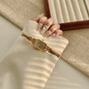 A close-up of a gold-toned quartz fashion wristwatch worn on a hand, resting on a beige fabric surface.