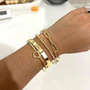 A hand wearing a stack of dainty gold plated bracelets on the wrist.