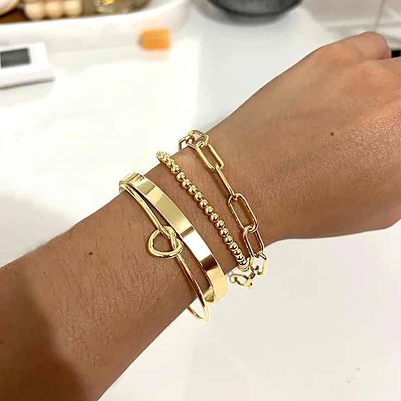 A hand wearing a stack of dainty gold plated bracelets on the wrist.
