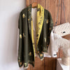 A dark olive green pashmina shawl with a yellow floral print lining displayed on a wooden background.