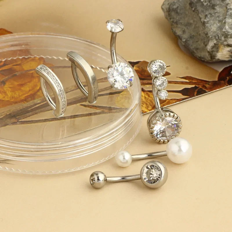 A collection of surgical stainless steel belly button rings and piercings displayed on a clear plastic dish.