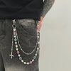 A silver chain necklace featuring various colored beads and a cross pendant is displayed against dark denim fabric.