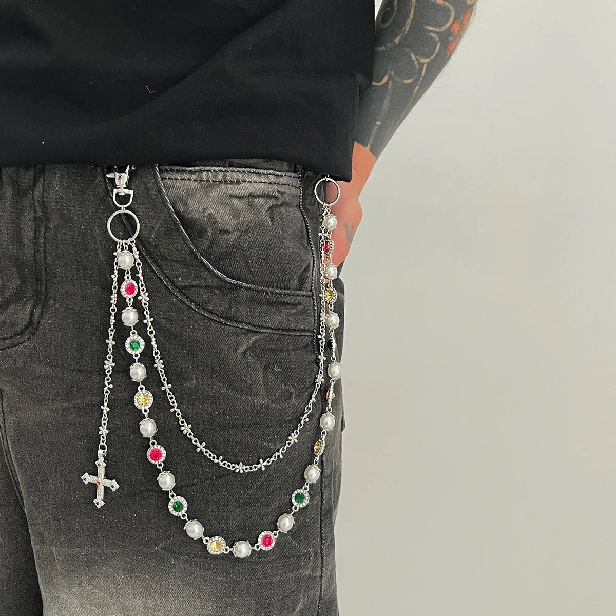 A silver chain necklace featuring various colored beads and a cross pendant is displayed against dark denim fabric.