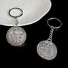 Silver round medallion keychain featuring a religious figure and Latin text on a white plate.