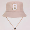 A light beige sun hat with a large gold letter B embroidered on the front.