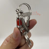 Un porte-clés mécanique en acier inoxydable avec une perle rouge et des fils enroulés est tenu dans une main.
