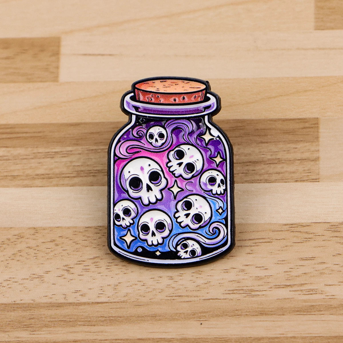 A dark purple enamel pin featuring multiple white skulls and swirling patterns, set in a glass-like container.