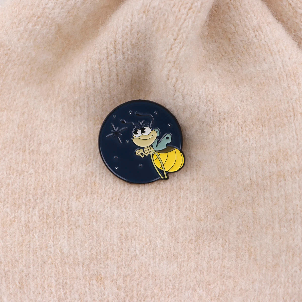 A dark blue enamel pin featuring a cartoon firefly frog brooch on a light beige fabric background.