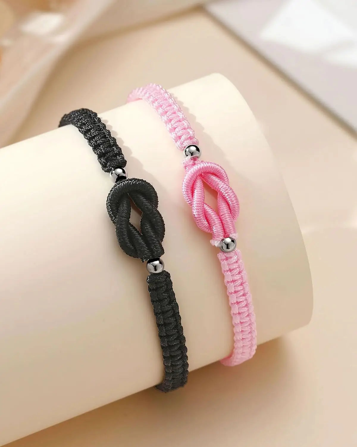 Two beaded bracelets, one black and one pink, are displayed on a wrist.