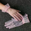 Pink lace tulle finger gloves being worn on a hand against a dark gray fabric background.