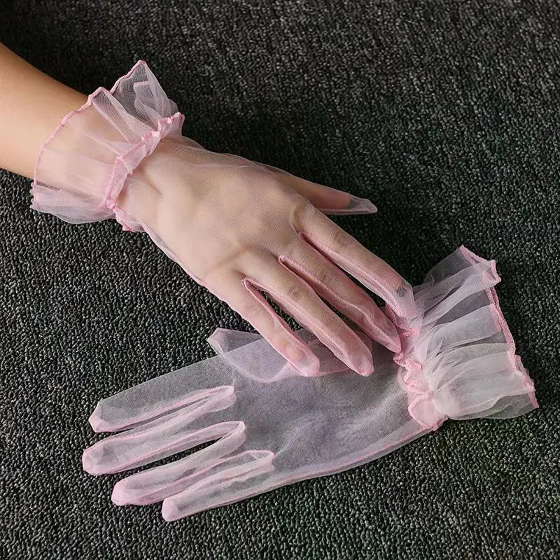 Pink lace tulle finger gloves being worn on a hand against a dark gray fabric background.