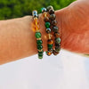 Une main porte plusieurs bracelets perlés faits de pierres de citrine et d'œil de tigre.