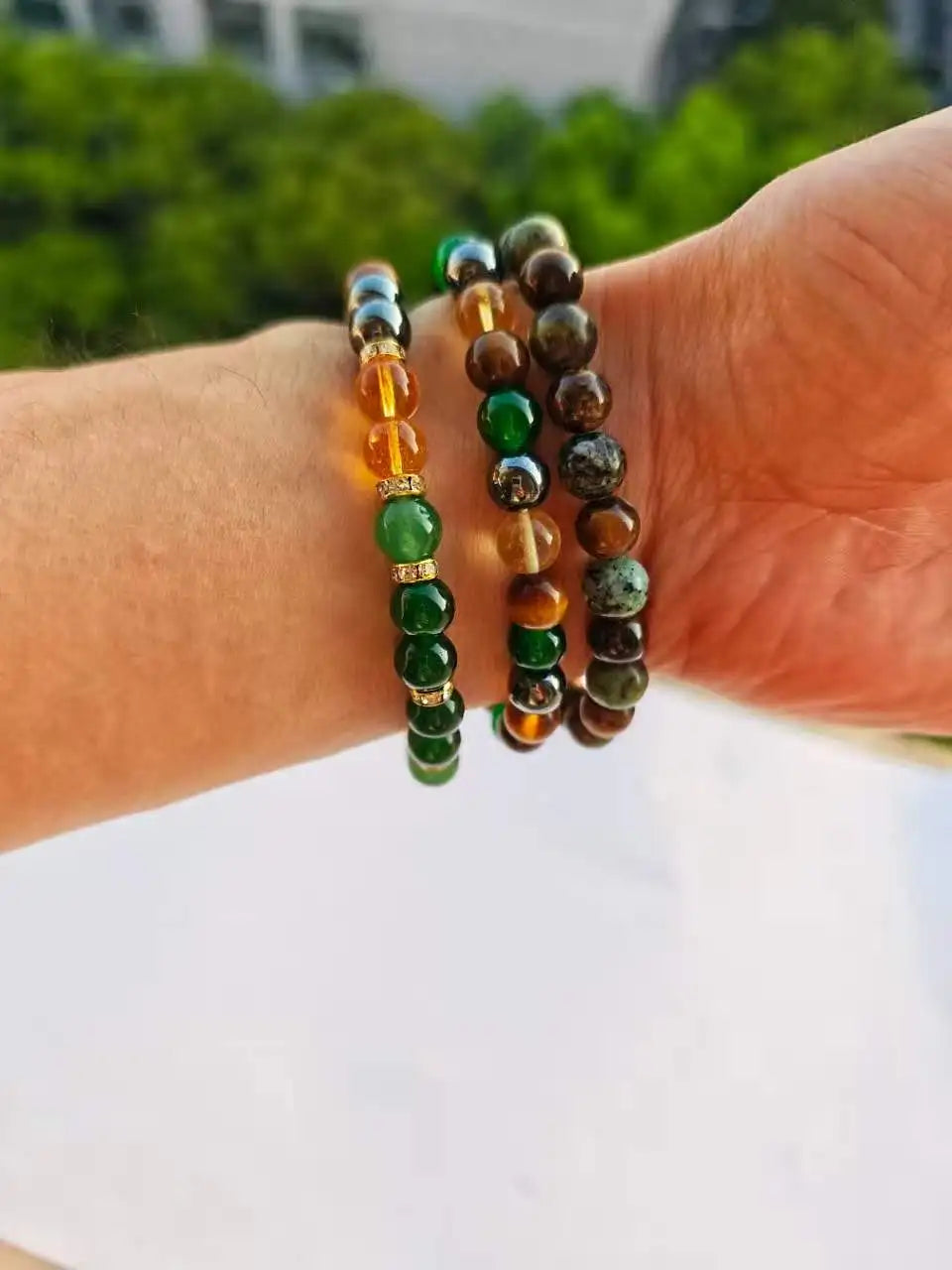 Une main porte plusieurs bracelets perlés faits de pierres de citrine et d'œil de tigre.