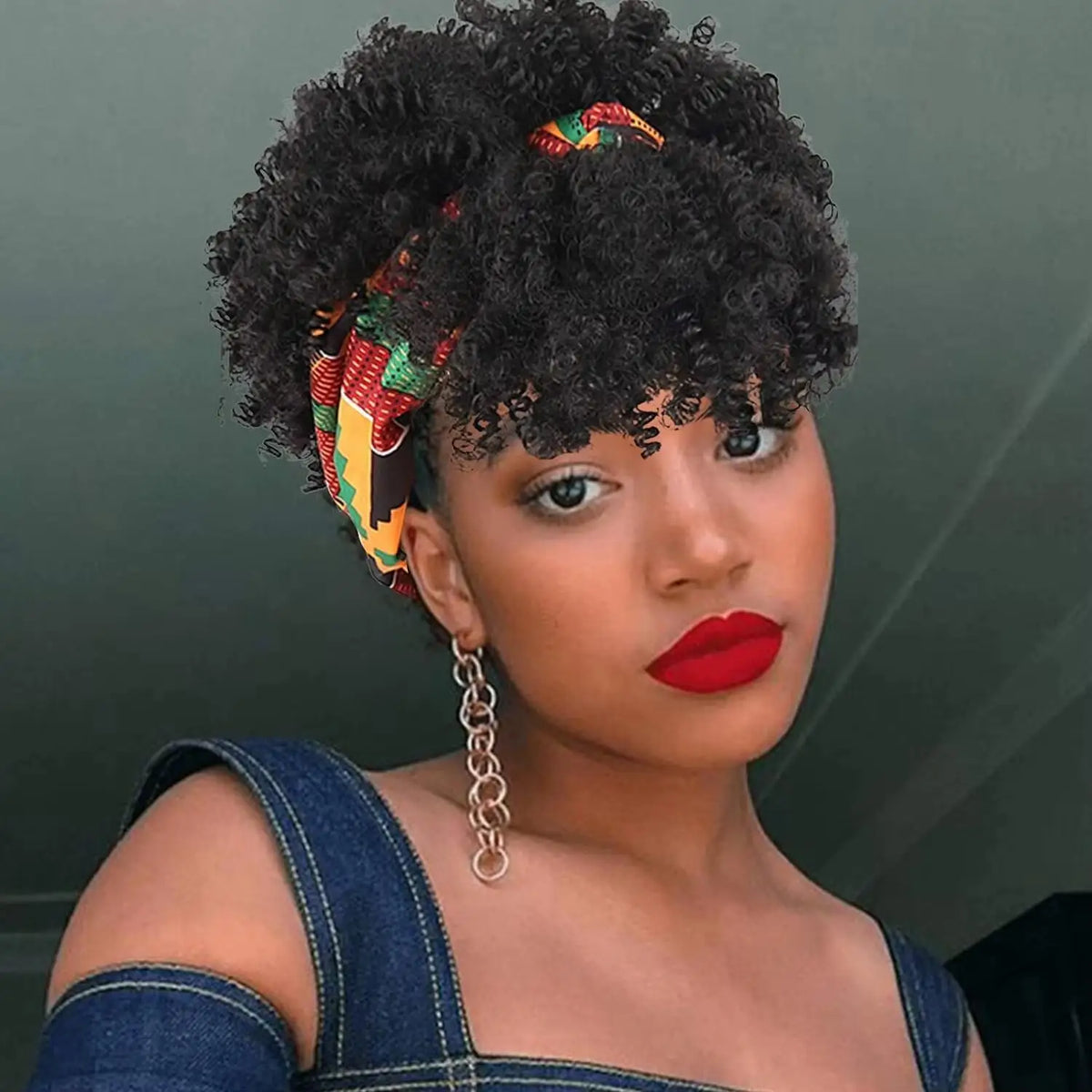 Una mujer vistiendo una peluca afro rizada negra con una diadema estampada colorida y lápiz labial rojo.