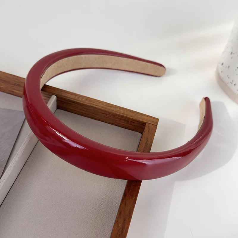 A glossy red PU leather fashion headband is displayed on a wooden stand.
