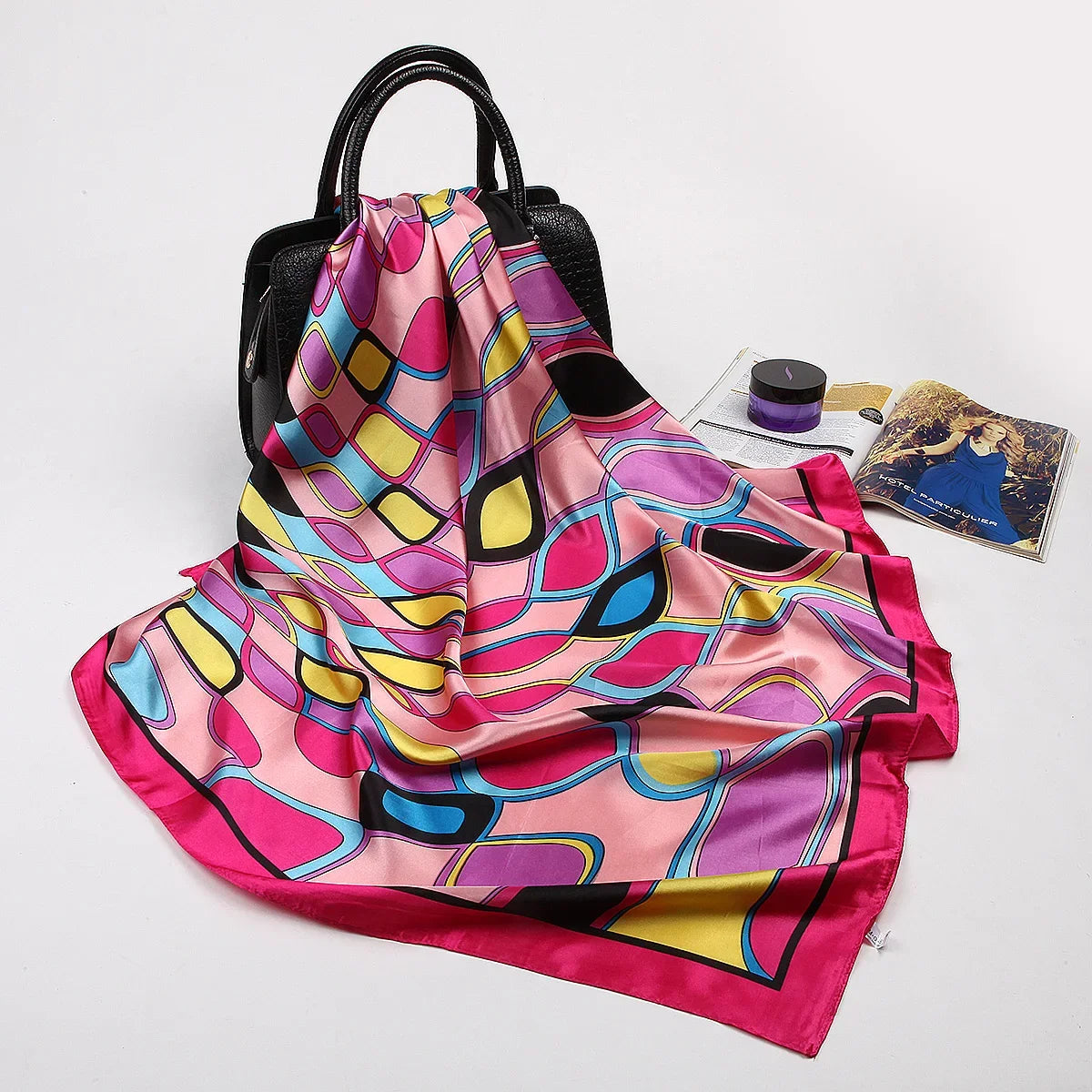 Leuchtend rosa und lila Seiden-Satin-Hijab-Schal über einer schwarzen Tasche drapiert.