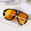 Un par de gafas de piloto vintage grandes con montura negra y lentes ámbar sobre una superficie blanca junto a una texturizad