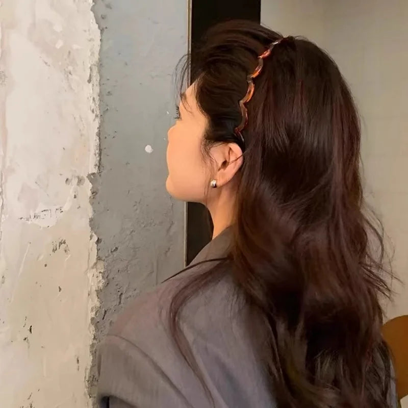 A woman with long dark hair is shown from the side, wearing a textured hair band.