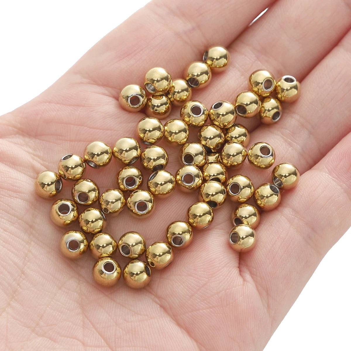 A hand holds a cluster of small, round gold-colored spacer beads for DIY jewelry making.