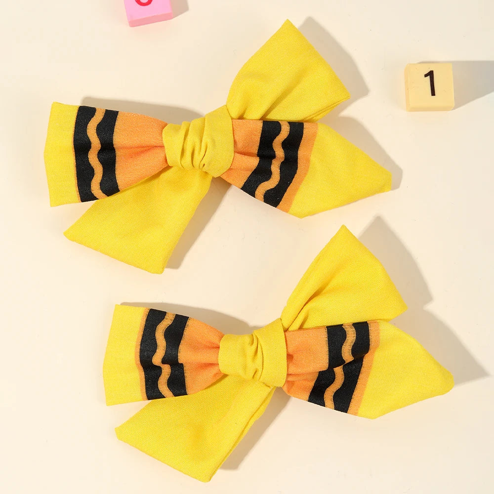 A set of yellow pencil bow hair clips featuring black and orange stripes.