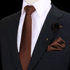 Chaqueta oscura con camisa blanca, corbata de seda marrón y un prendido floral oscuro en la solapa.