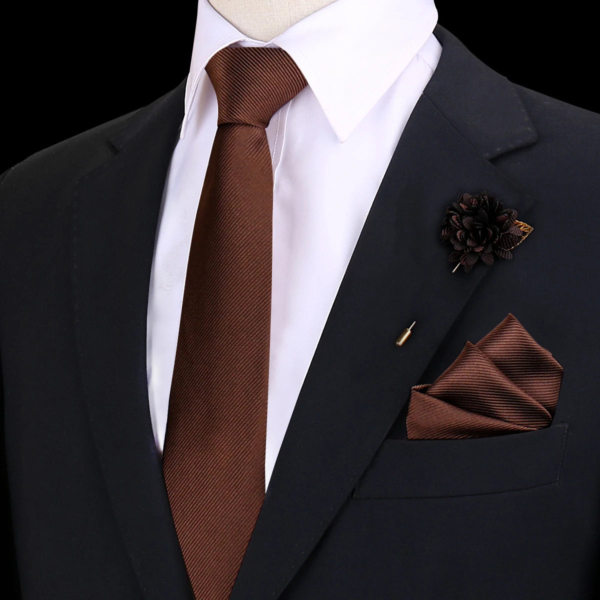 Chaqueta oscura con camisa blanca, corbata de seda marrón y un prendido floral oscuro en la solapa.