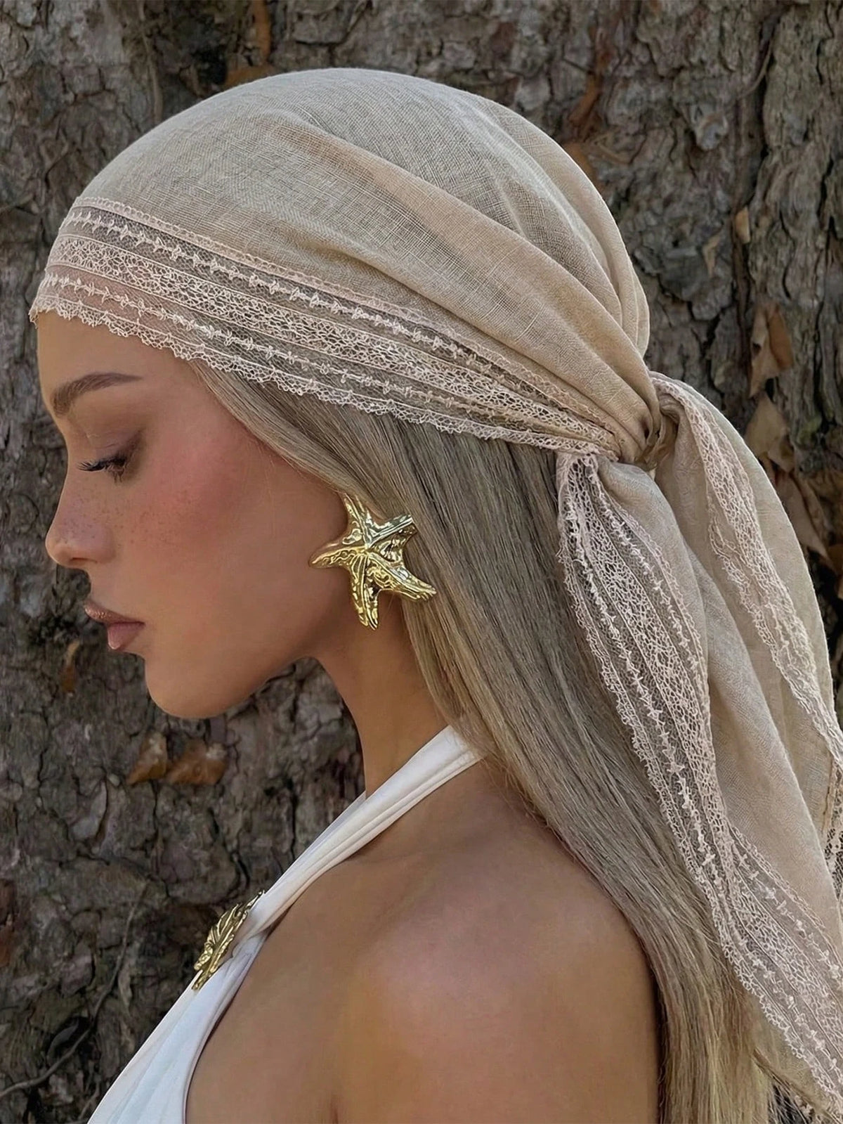 A woman wearing a beige bohemian lace trim shawl draped over her head and hair, featuring a gold starfish earring.