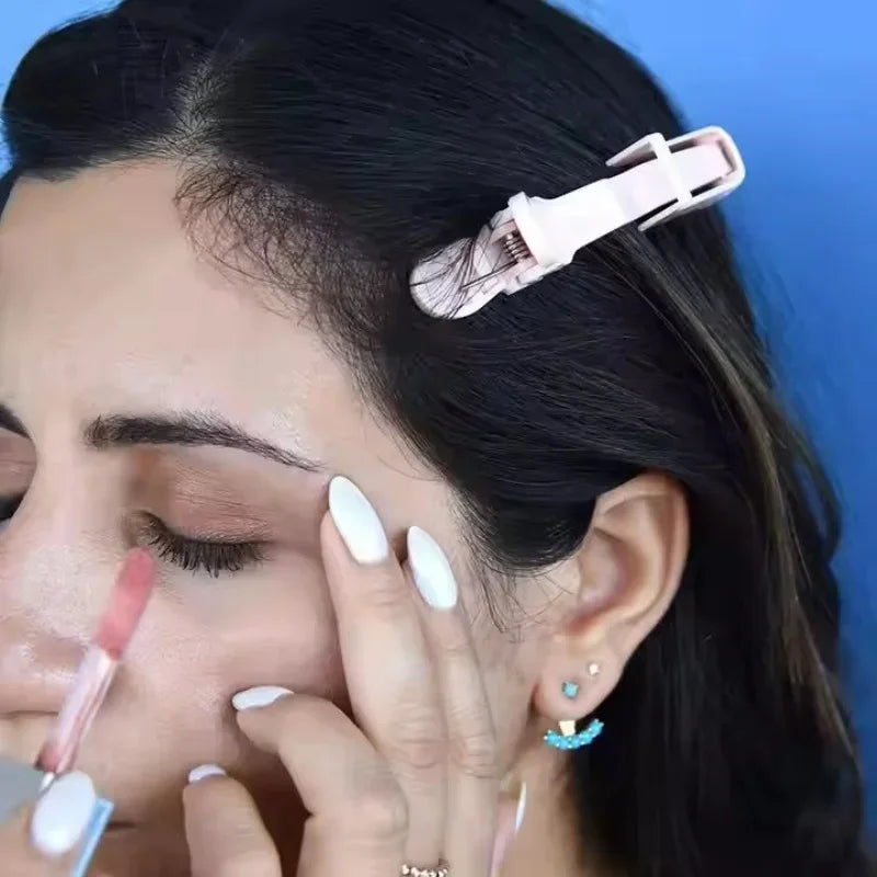 A close-up of a person using pink alligator hair sectioning clips on their dark hair.