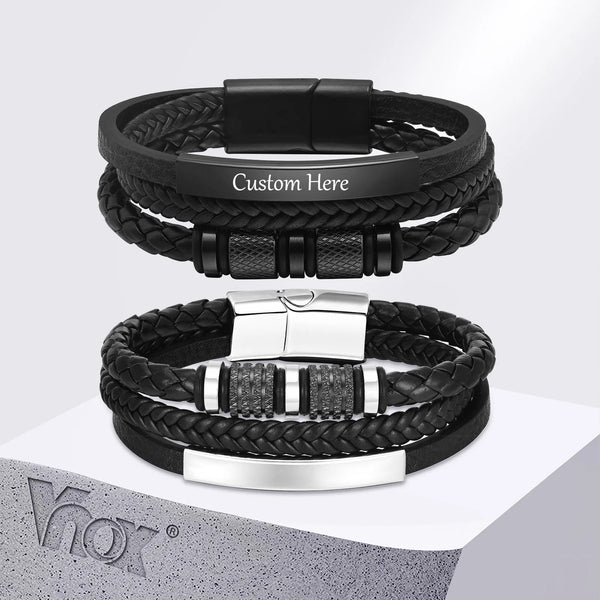 A black braided leather bracelet with a silver buckle and custom engraving is displayed on a white surface.