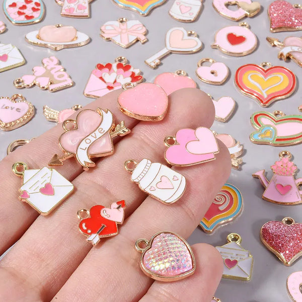 A hand displays various assorted enamel charms, including hearts and other shapes, for DIY jewelry making.