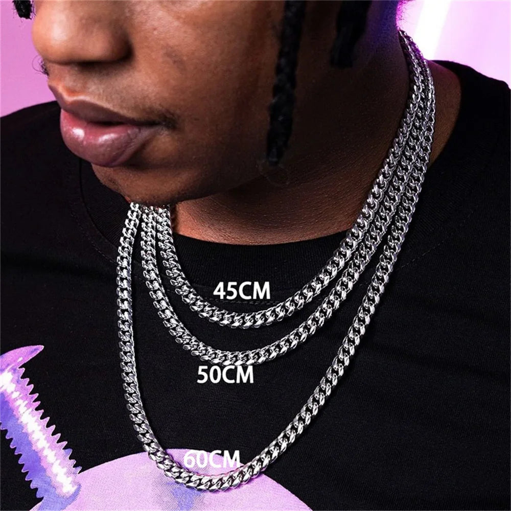 Close-up of a man wearing multiple stainless steel Cuban chain necklaces of varying lengths around his neck.